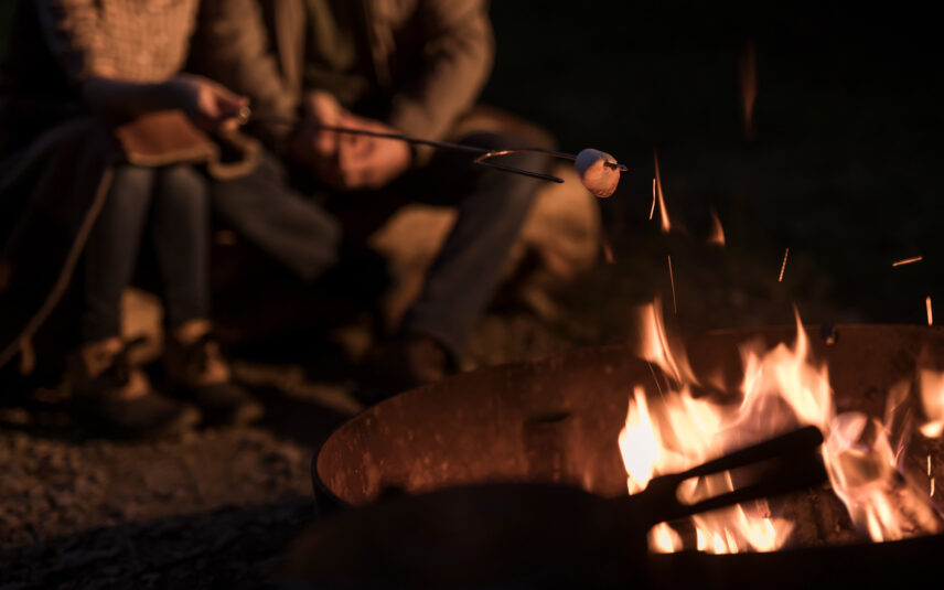 Close-up of a vibrant, crackling campfire with orange and yellow flames in a stone fire pit, surrounded by gravel, at Gateway Lodge in Cook Forest, Pennsylvania, ready for s'mores and outdoor enjoyment.