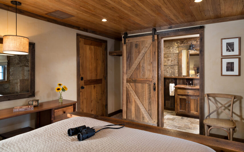 Inviting Gallery Room at Gateway Lodge in Cook Forest, Pennsylvania, featuring a wooden door, a vase of bright yellow sunflowers on a rustic table, and black binoculars resting on a comfortable bed, suggesting a nature-lover's retreat.