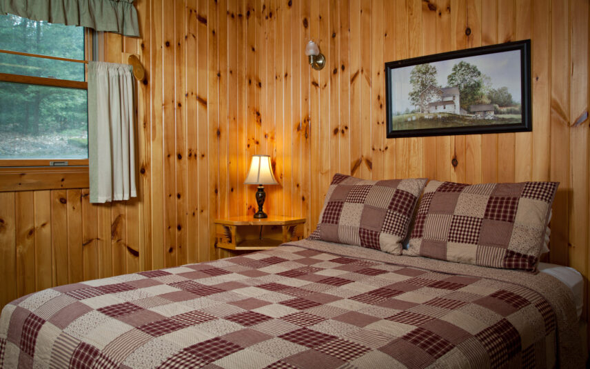Queen bed with a patchwork quilt in a cozy bedroom with wooden walls inside a Black Bear Cabin at Gateway Lodge in Cook Forest, Pennsylvania.