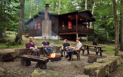 four friends gathering around a campfire behind a cabin