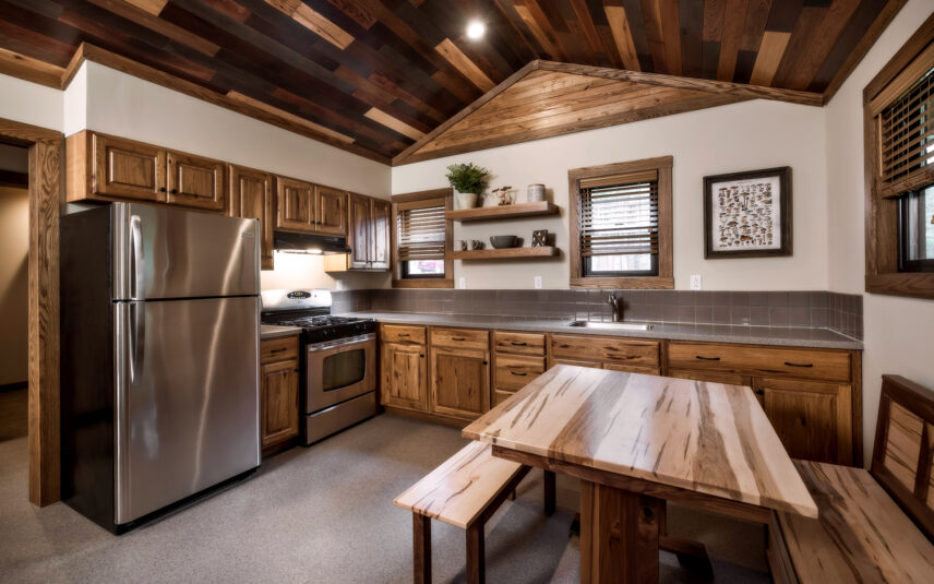 Kitchen in the ADA-accessible Cook Cabin at Gateway Lodge, Cook Forest State Park, Pennsylvania, featuring wooden cabinetry, a full-sized refrigerator, stove, sink with accessible counter space, and a dining table with benches, designed for ease of use.