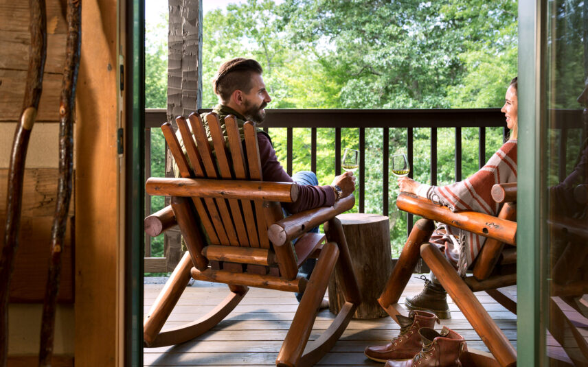 Couple enjoying a conversation on a suite balcony at Gateway Lodge in Cook Forest, Pennsylvania, holding wine glasses of white wine, with a scenic outdoor view.