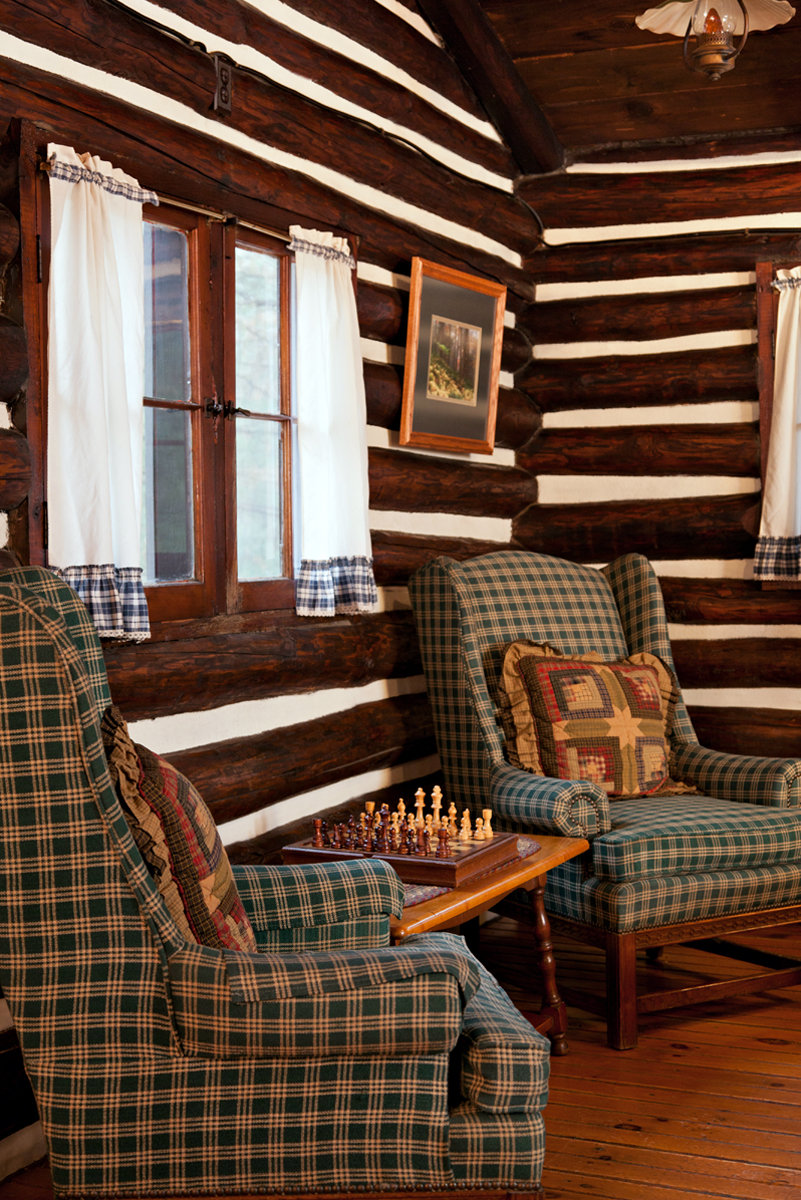 Two plaid armchairs facing each other with a chessboard on a small table between them in the living area of a Hemlock Cabin at Gateway Lodge in Cook Forest, Pennsylvania, featuring rustic log beam walls.