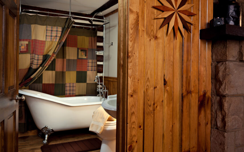 Clawfoot bathtub with plaid shower curtain in the private bathroom of a Hemlock Cabin at Gateway Lodge in Cook Forest State Park, Pennsylvania. Rustic cabin bathroom with a classic pedestal tub for a relaxing soak during your Pennsylvania getaway.