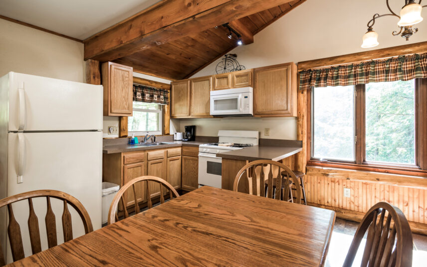 Kitchen in a Longfellow Cabin at Gateway Lodge in Cook Forest, Pennsylvania, featuring light wood cabinets, white appliances (refrigerator, microwave, stove), a sink, and a wooden dining table with four chairs.
