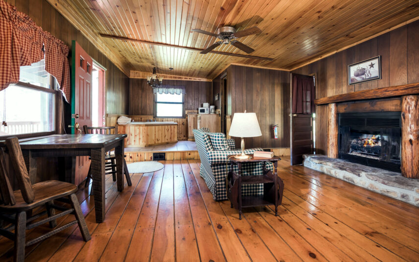 Living room area in the Red Eft Cabin at Gateway Lodge in Cook Forest, Pennsylvania, featuring a lit gas fireplace with a rustic mantel, a built-in wooden jetted tub, a kitchenette area with a microwave, and a plaid armchair.