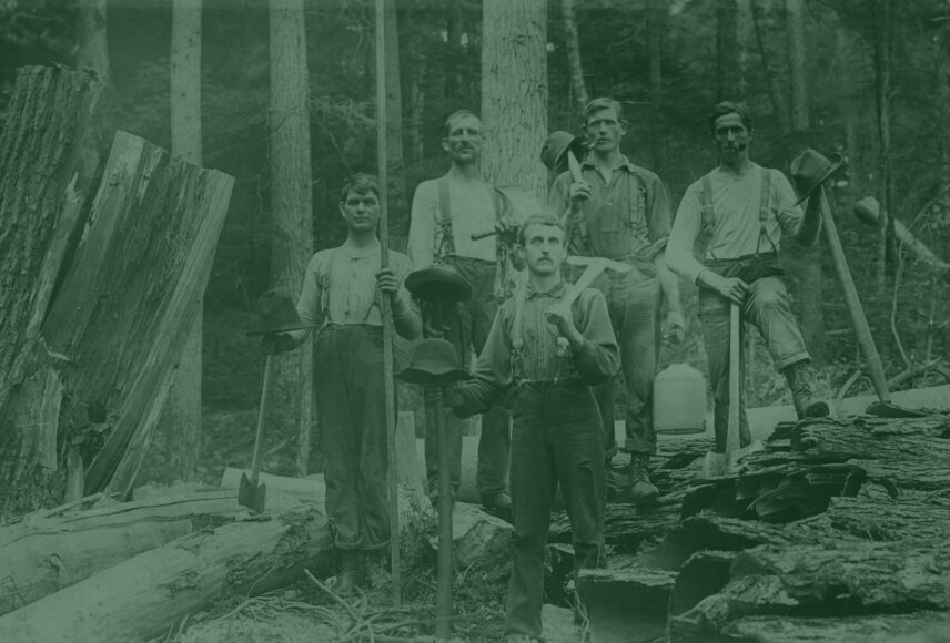 Vintage photograph of five lumberjacks standing amongst large felled trees in what appears to be a forest in Cook Forest, Pennsylvania. Each man is holding or has an axe nearby, and several have hats resting on the handles of their tools. They are dressed in work clothes typical of the logging era. The backdrop of tall trees and remnants of logging activity emphasizes the historical significance of the lumber industry in the region surrounding Cook Forest State Park. This image offers a glimpse into the hardworking past of the area, a history that adds to the rich heritage near Gateway Lodge.