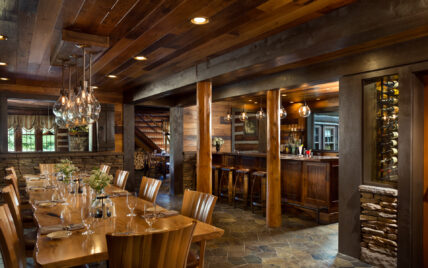 Gateway Lodge bar with long silver wormy maple table on left, bar seating on right with wine barrel stools, partial view of wine cellar, showing a variety of wooden interior architecture