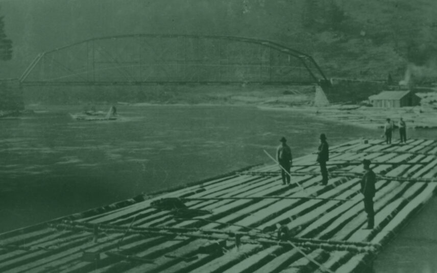 Vintage photograph of four men maneuvering a long, flat-bottomed raft of logs down the flowing Clarion River in Cook Forest State Park, Pennsylvania. A substantial steel truss bridge spans the river in the hazy background, suggesting a journey towards Pittsburgh's industrial past. The men, dressed in dark, period-appropriate clothing and hats, use long poles to navigate the waterway. The river reflects the muted tones of the sky and surrounding forested landscape. This historical image evokes a sense of early transportation and logging history relevant to the Clarion River and the region surrounding Gateway Lodge.