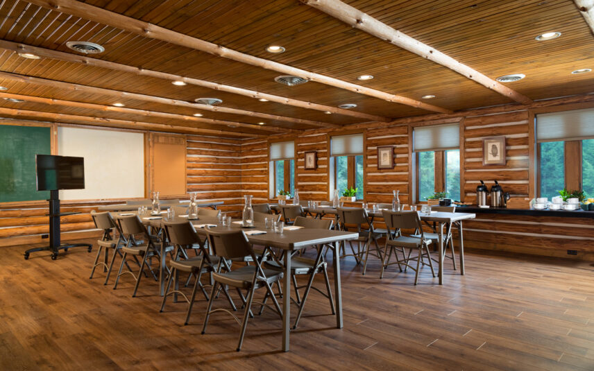 Interior of the spacious meeting room at the Forest Meeting Facility and Retreat Center, Gateway Lodge in Cook Forest, Pennsylvania, showcasing a wooden interior, flexible table setup, a rollaway TV cart for presentations, and a well-stocked food, tea, and coffee bar.