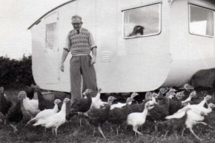 A man standing among wild turkeys in front of his camper.
