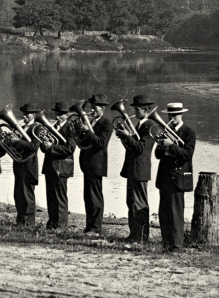 vintage black and white photo of five musicians wearing top hats, playing trumpets near the Clarion River in Cook Forest State Park, Pennsylvania