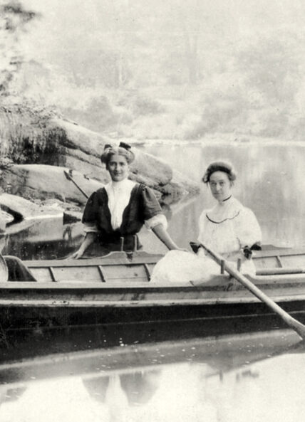 vintage black and white photo of two woman wearing long dresses in a wooden canoe on the Clarion River in Cook Forest State Park, Pennsylvania