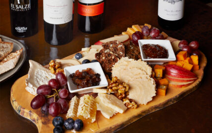 cheese and fruit platter featuring a selection of Red Rock, Leonora, and Prairie Breeze cheeses, accompanied by a seasonal array of fresh fruits, Tait Farm preserves, Marcona almonds, toasted baguette, and rustic crackers