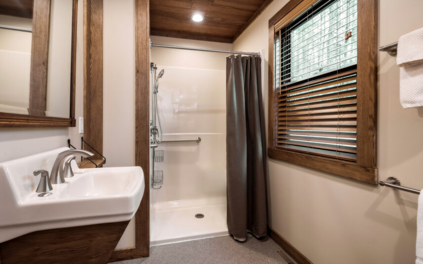 A handicap accessible bathroom in a Cook Cabin at Gateway Lodge in Cook Forest State Park, Pennsylvania, featuring a walk-in shower with handrails and a lowered sink.