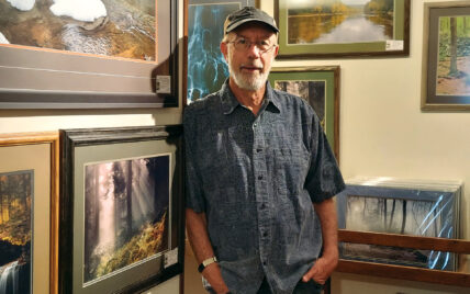 portrait of nature photographer Kevin Kaltenbaugh in his gallery, with framed nature photographs in the background