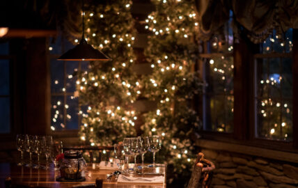 table setting in the dining room at Gateway Lodge adorned with wine glasses against a backdrop of twinkling Christmas lights