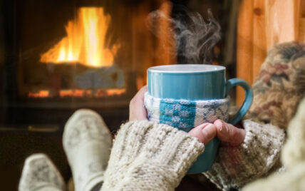 Woman holding coffee in front of fireplace advertising our Hygge in the Wilds package for January