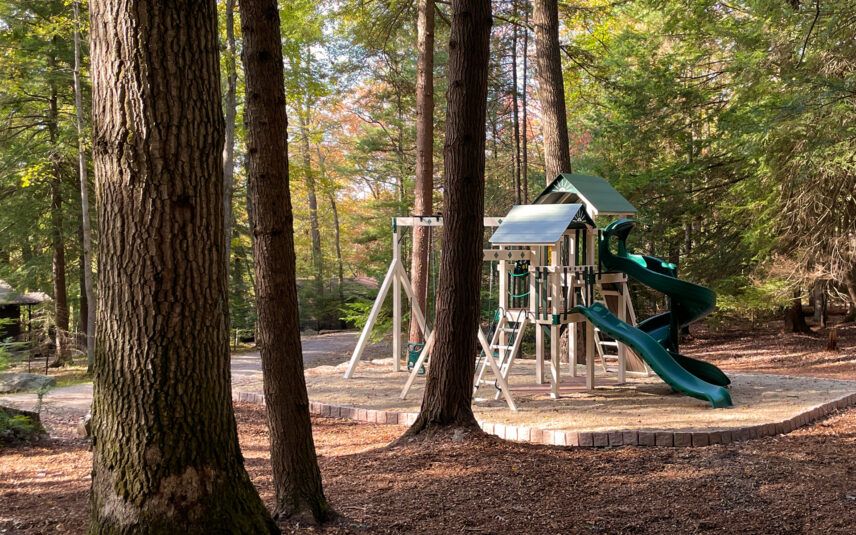 A well-maintained playground area with swings and slides nestled among the trees at Black Bear Cabins in Cook Forest State Park, Pennsylvania, a family-friendly lodging option near Gateway Lodge.
