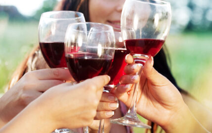 Close-up of multiple hands clinking wine glasses filled with red wine outdoors, symbolizing celebration and fine dining experiences available at Gateway Lodge in Cook Forest, Pennsylvania.