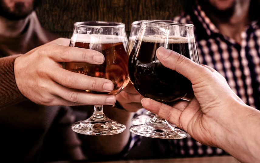 Close-up of hands toasting with glasses of craft beer, including a lighter and a dark stout, from Bark Brew at Gateway Lodge in Cook Forest, Pennsylvania, symbolizing enjoyable social gatherings and on-site beverage experiences.